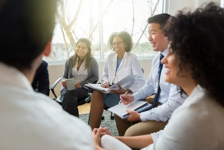 Patient care team in a hospital sitting at a casual meeting, smiling and laughing.