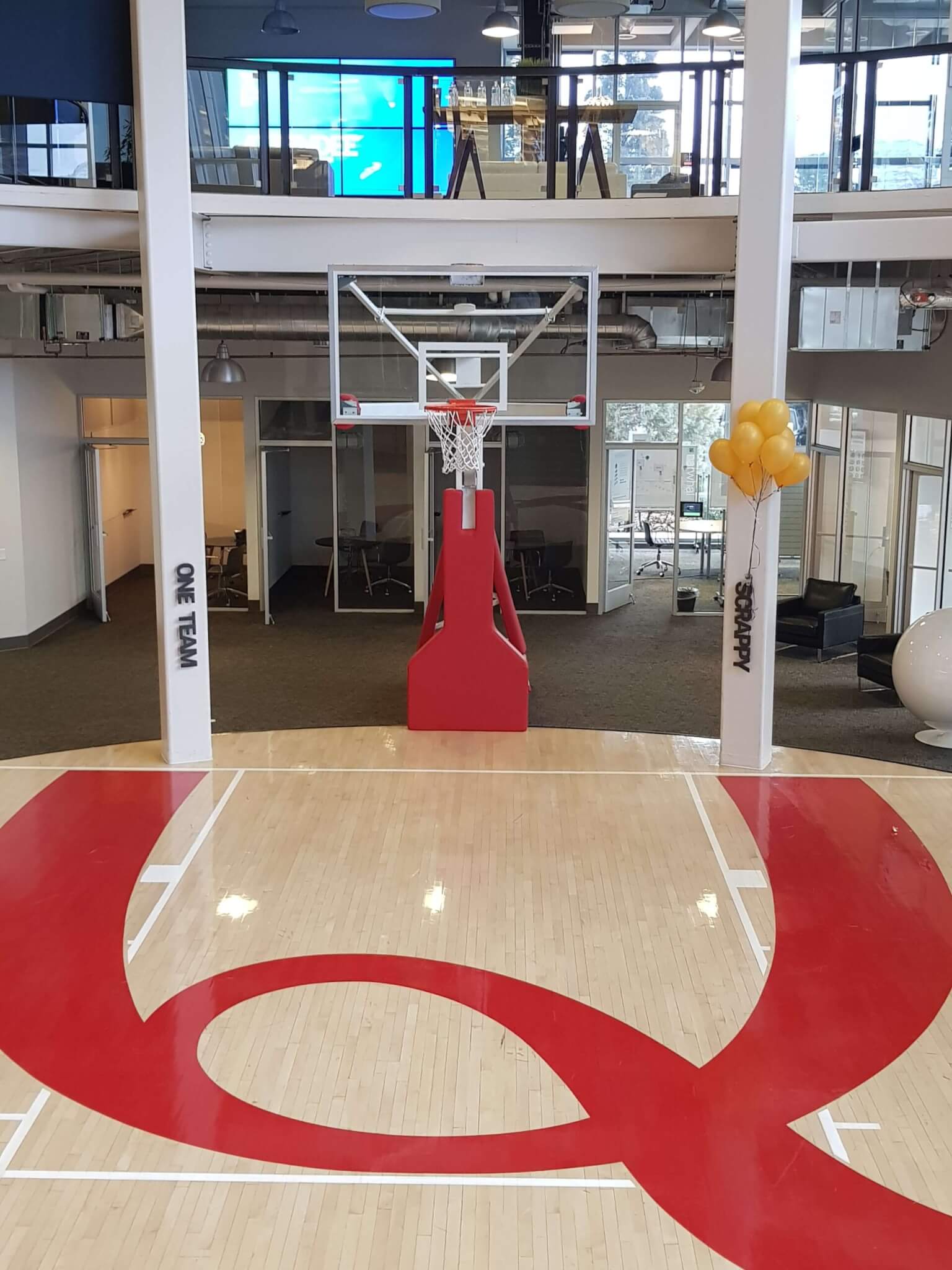 The Qualtrics Provo HQ main entry, which features a basketball court with a giant red letter Q on the floor. PIctured also is 2 of the 5 TACOS pillars - One Team & Scrappy