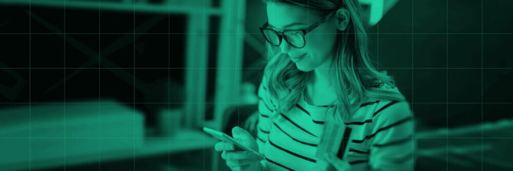 Woman with glasses looking at her phone while holding credit card