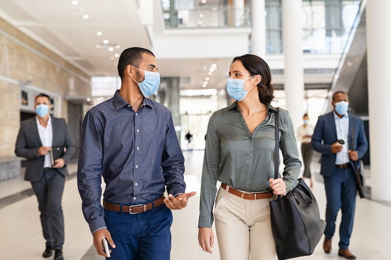 Colleagues wearing face masks walking together in office building