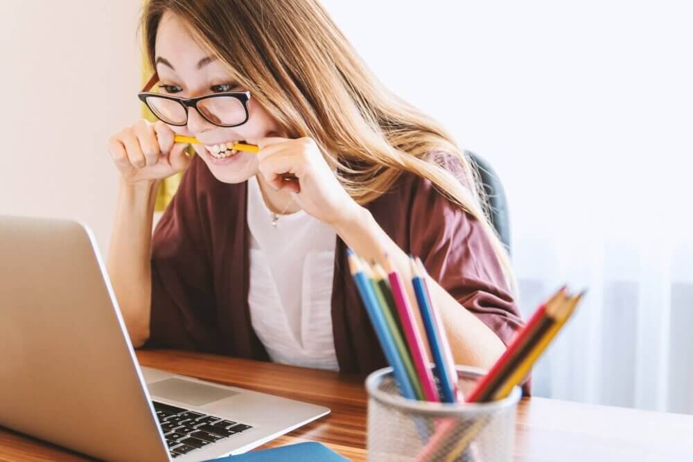 Woman with glasses at laptop nervously biting a pencil