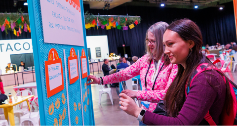 Two attendees interacting with colorful activity board at X4 Summit networking area