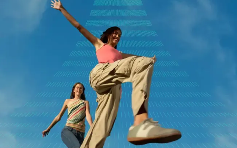 Two women walking outdoors against a blue sky, with one jumping energetically, overlaid with Qualtrics signal graphics.