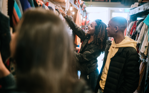 Two people browsing clothing racks together in a retail store, smiling and engaged.