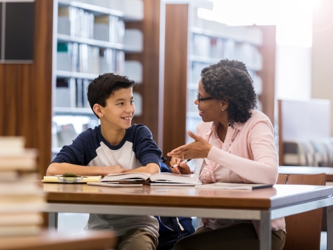 A student and educator talking at a table in a school library
