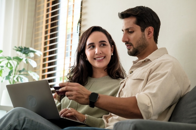 Couple sitting on couch at home buying something online on their laptop