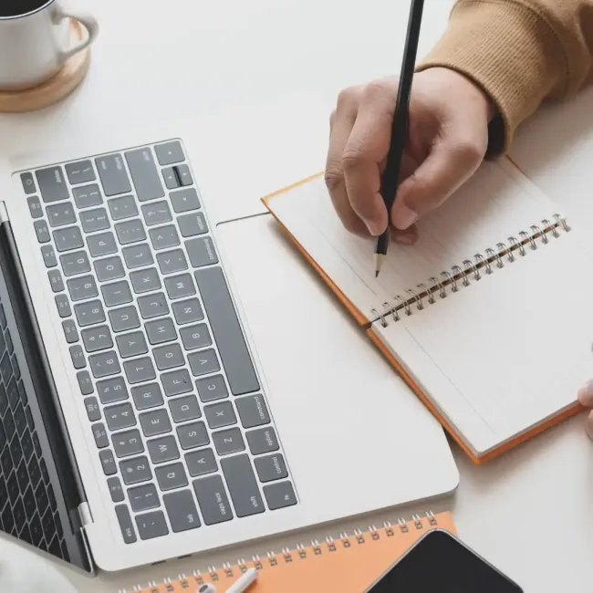 Person writing in notebook over laptop trackpad