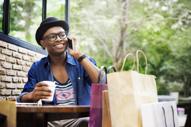 Man drinking a coffee and talking on his phone with shopping bags next to him.