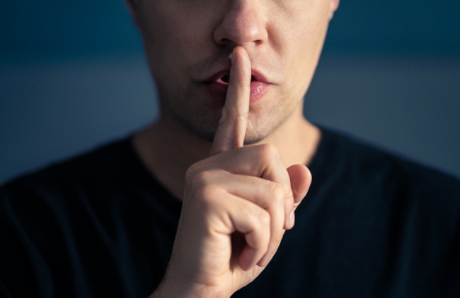 Man making shhh / quiet gesture by placing his index finger to his lips.