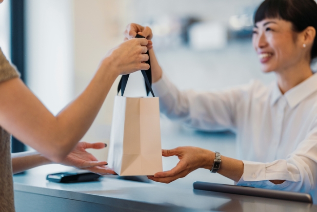 Cashier handing over bag to smiling woman at checkout in store.