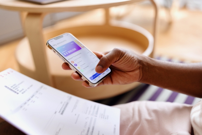 Person paying bills online through a mobile banking app while looking at their bank statement.