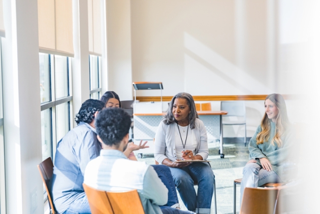 A group of adults and an older female sitting in a circle during a group meeting session.