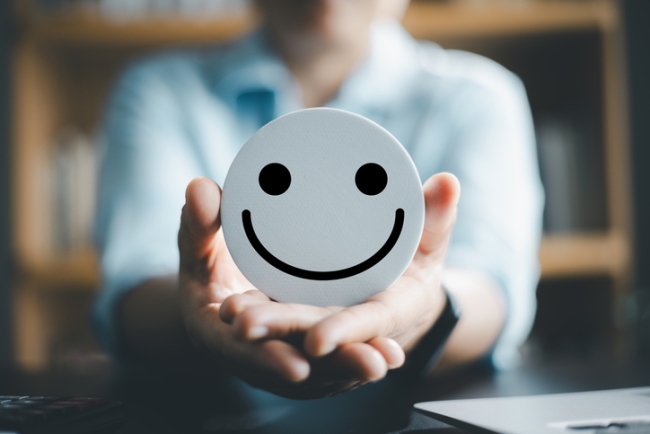 Woman, blurred, holding out an in-focus smiley face. 