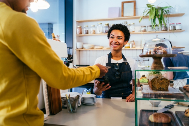  Smiling barista or store clerk accepting payment from a customer across a counter in a bright cafe.