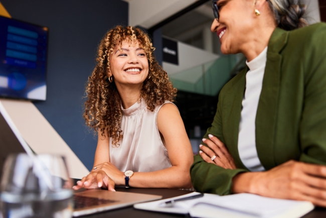 Two women engaged in friendly professional conversation at office meeting