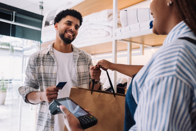 Man smiling while paying for a purchase with a credit card at a store.