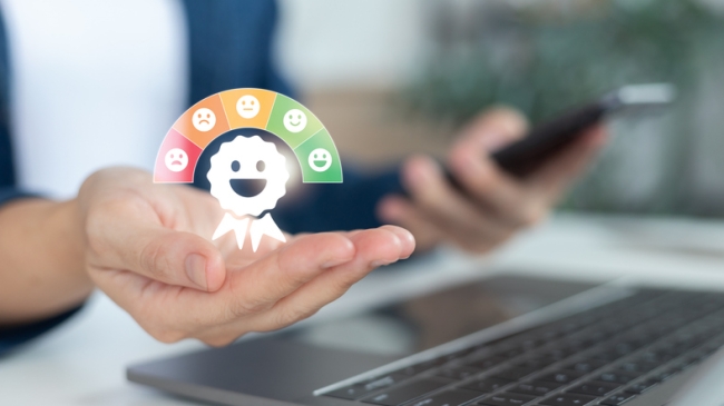 Hand presenting customer satisfaction rating concept with happy emoji and colorful satisfaction scale, with laptop and smartphone in background