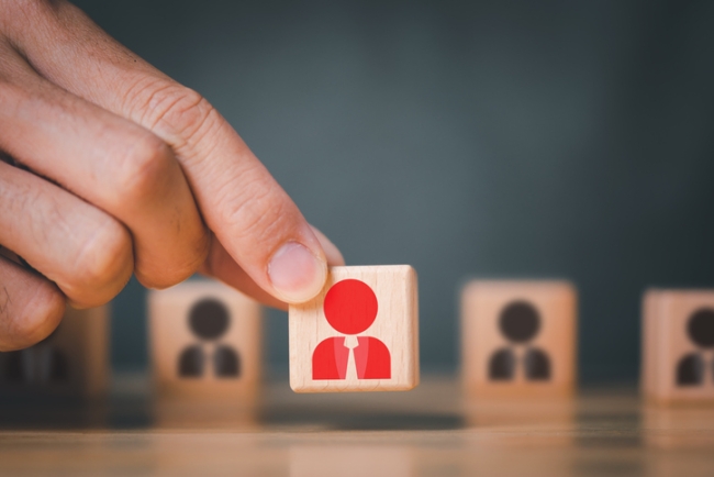 Hand selecting wooden cube from selection with illustration of person in red.