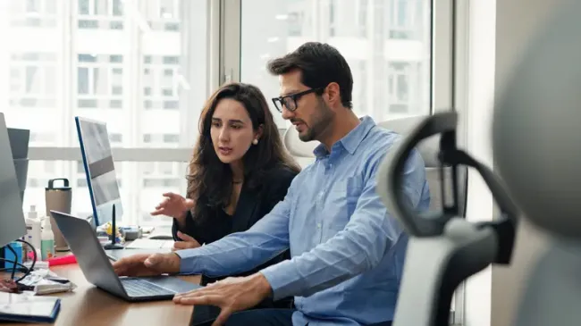 Two coworkers talking, pointing at a laptop in an office building