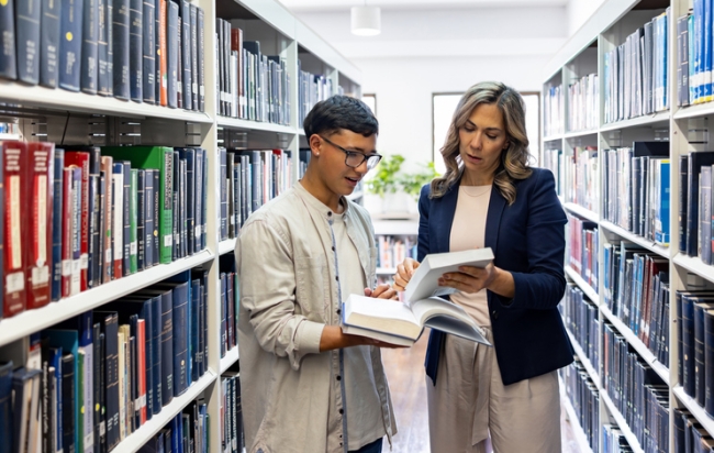 Students or colleagues collaborating on research in library between bookshelves
