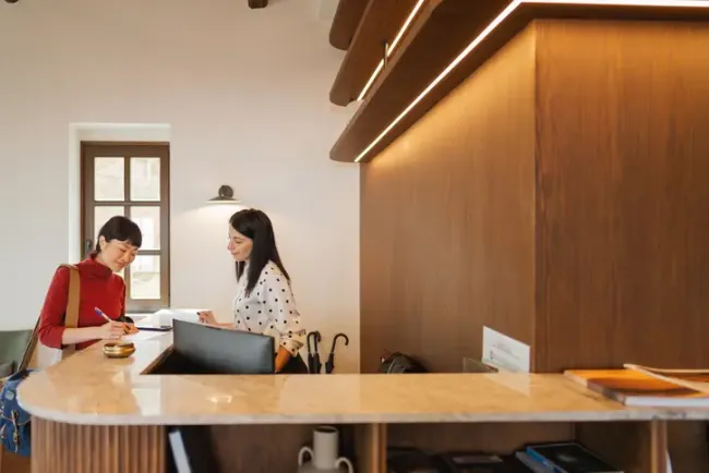 ホテルのフロントでスタッフに案内されながら書類に記入する宿泊客。