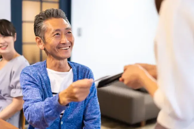 カジュアルなグループの集まりでタブレットを手渡しながら微笑む男性。