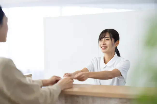 カウンター越しに来訪者にカードを手渡しながら微笑む受付スタッフ。