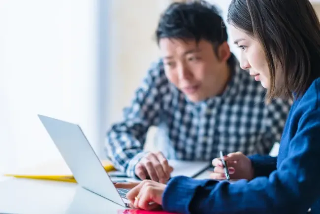 共有デスクで一緒にノートパソコンの画面に集中する2人の同僚。