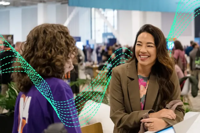 Two attendees having a conversation at the Qualtrics X4 conference, with one person smiling warmly while facing the other in a busy expo hall setting.