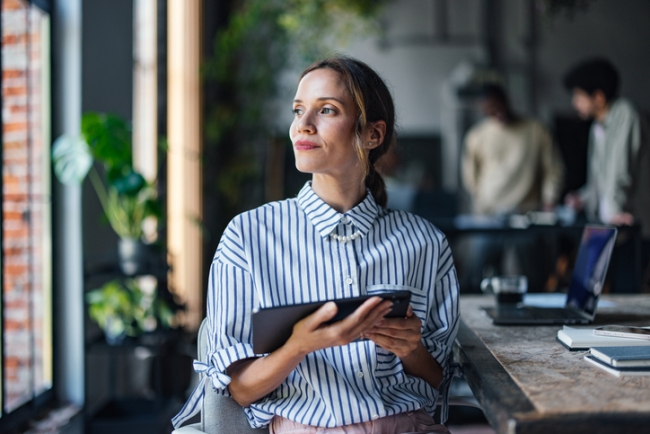 A thoughtful woman holding a tablet and looking off-camera, representing a customer engaging deeply with a conversational survey.