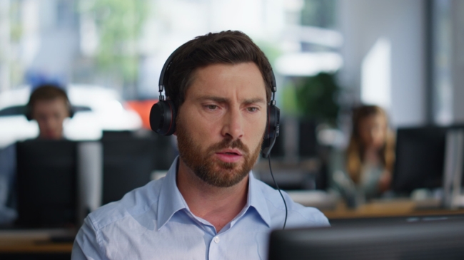Male call center agent with headset talking to a customer on the phone.