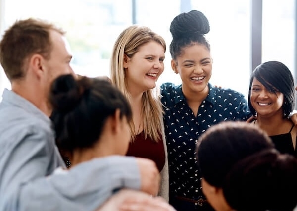 Group of colleagues smiling, laughing and embracing in circle.
