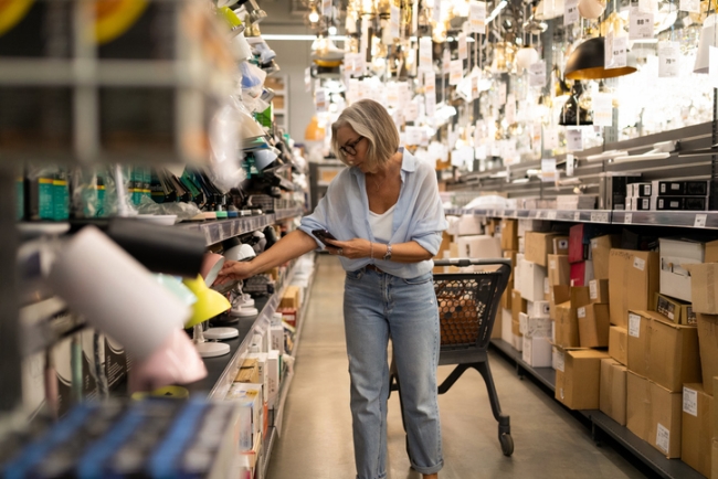 A woman with short gray hair browses through a crowded home decor store, examining colorful light fixtures. 