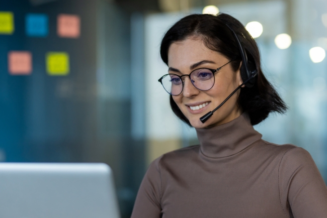 Smiling contact center rep wearing a headset and glasses engaging in a call.