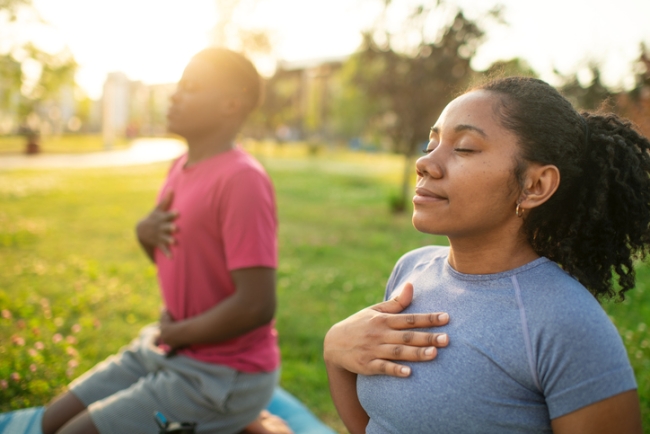 Young couple practicing yoga in a summer park, doing breathing exercise.