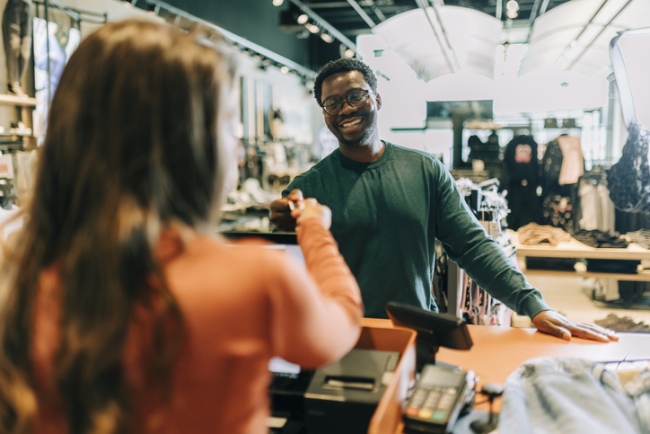 Clothing store owner handing a happy male customer a shopping bag with his purchase.