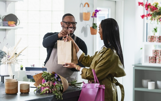 Man working at the checkout counter of a gift and flower shop, helping a customer make a purchase.