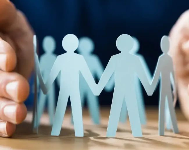 Paper chain of people holding hands being protected by human hands.