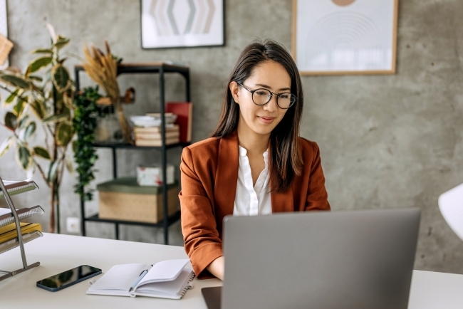 Stock image of an east asian woman sitting at a desk working at a laptop