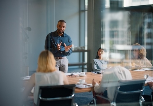 Stock image of a black man presenting to a group of professionals in a conference room