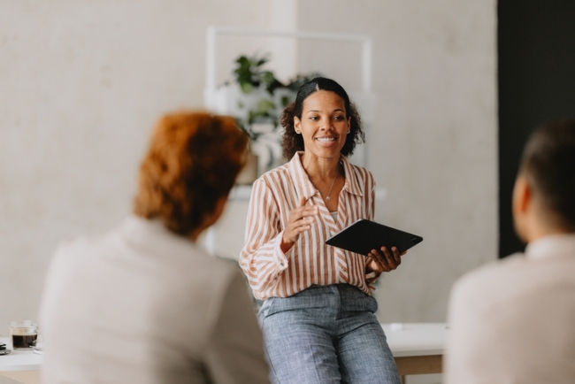 Stock image of a young black woman holding a tablet talking with colleagues