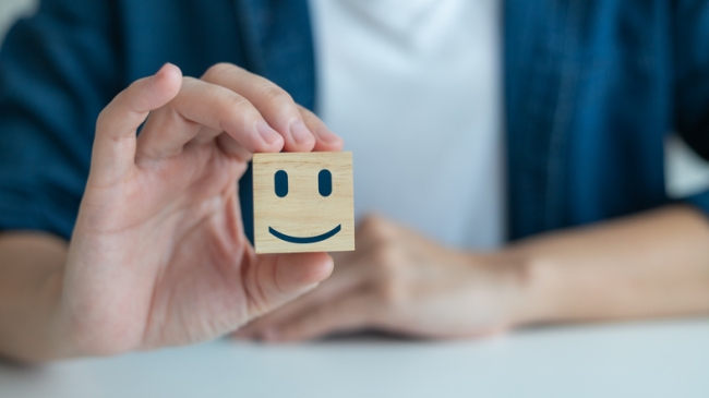 Man holding a small wooden block with a smily face painted on it.
