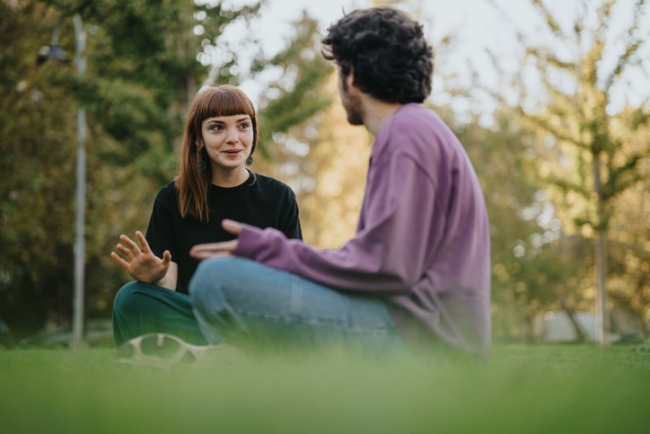2 young friends sitting on grass, enjoying a conversation outdoors.