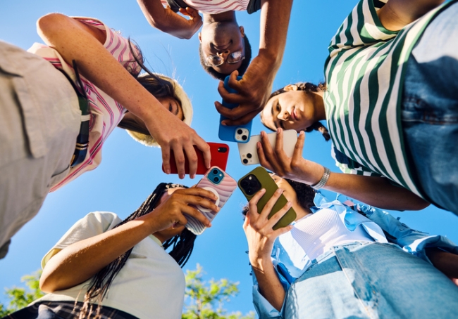 Group of teenagers using smartphones  to look at social media outdoors.