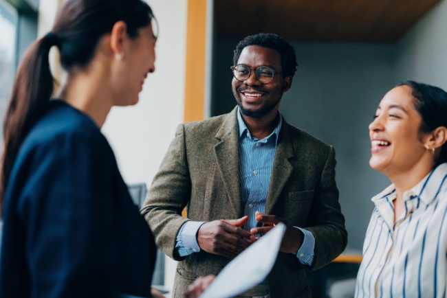 Three diverse professionals smiling and talking in an office setting.