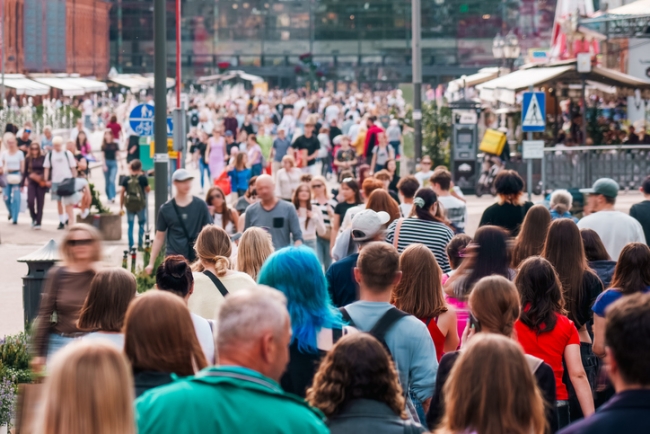 Large group of people walking in busy downtown area on a sunny day, reflecting vibrant city atmosphere and diverse population.
