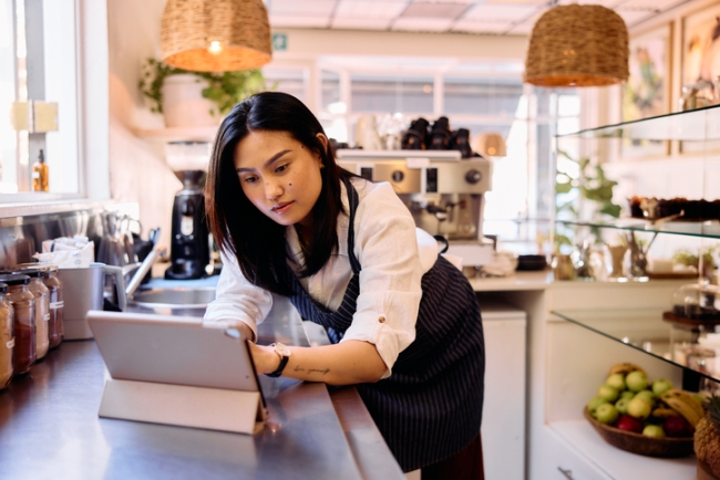 Female employee in her 30s working in cafe using a digital tablet.