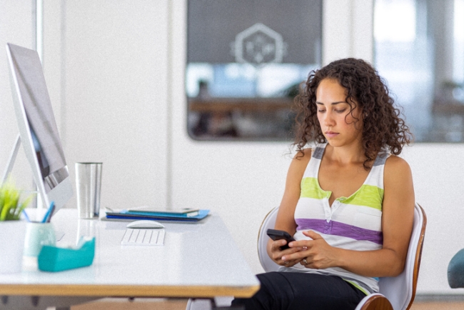 Disengaged young, female employee using their smart phone at work.