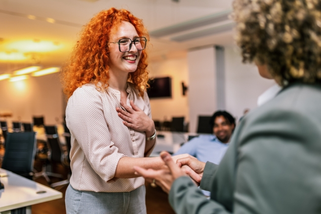 Team manager congratulates employee on their performance, shaking their hand and prompting applause from her coworkers.