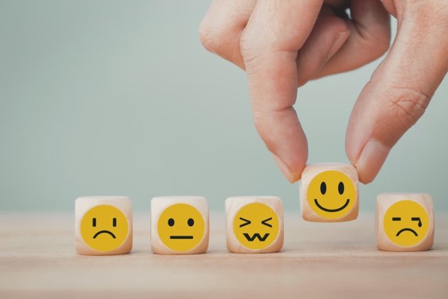 Hand chooses happy smile face emoticon icon from selection of wooden cubes—representing employee sentiment.